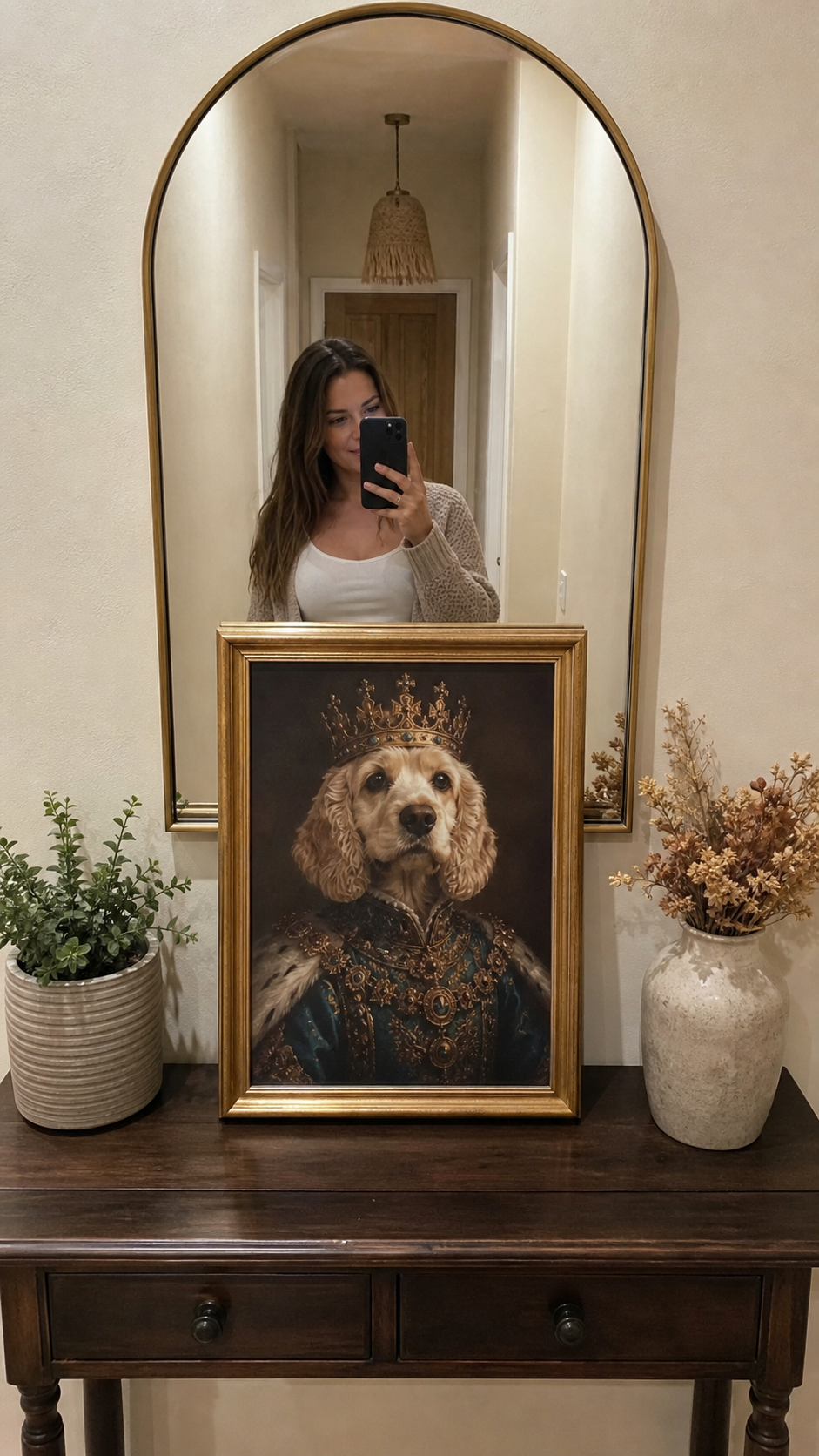 Woman taking a mirror selfie behind a framed dog portrait on a console table